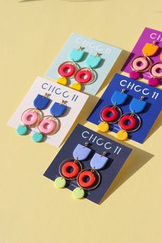 three pairs of colorful earrings on top of a yellow table next to cards with words