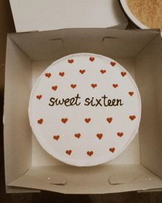 a cake in a box with the words sweet sixteen written on it and red hearts