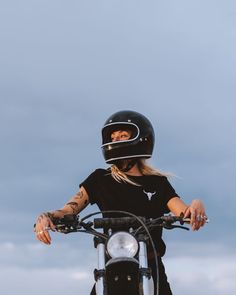 a woman wearing a black shirt and helmet sitting on a motorbike with the sky in the background