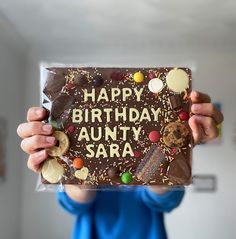 a person holding up a birthday cake with chocolate frosting and candies on it