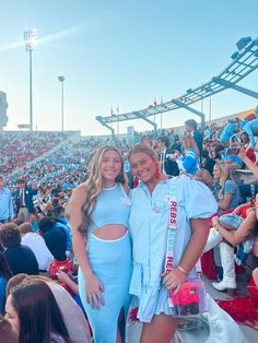 two women standing next to each other in front of a crowd at a sporting event