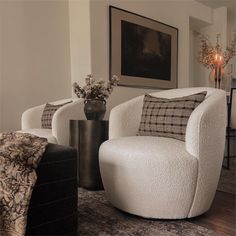 a living room with two white chairs and a vase on the table in front of it