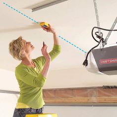 a woman is working on the ceiling in her garage with an electric device attached to the ceiling