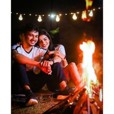 a man and woman sitting next to a campfire