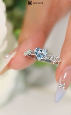 a woman's hand holding a ring with a heart shaped diamond on top of it