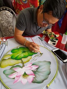 a man sitting at a table drawing on a plate with flowers and leaves painted on it