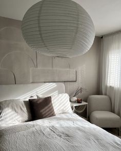 a white bed sitting next to a window in a bedroom under a large light fixture