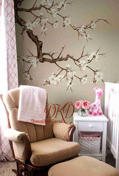 a baby's room with a tree painted on the wall and a chair in front of it