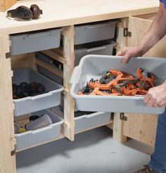 a man holding a plastic container filled with tools in his kitchen cabinet drawer, which is open to reveal the contents inside