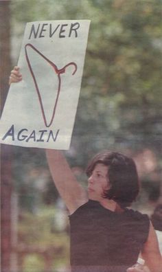 a woman holding up a sign that says never again against the right hand and an arrow drawn on it