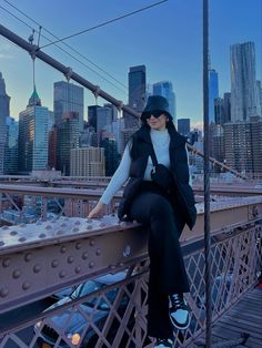 a woman sitting on the side of a bridge in front of a cityscape