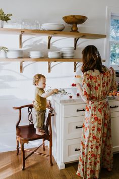 a woman standing in front of a kitchen sink with a toddler on the counter