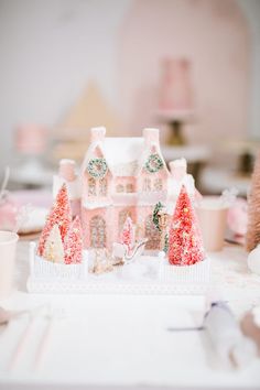 a pink and white christmas house on a table with other holiday decorating items in the background