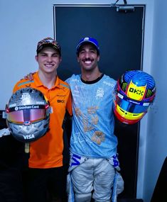 two men standing next to each other holding helmets