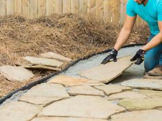 a man in blue shirt and black gloves working on a stone walkway