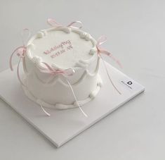 a white cake with pink ribbon on top