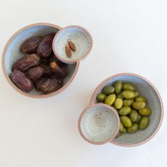 two bowls filled with different types of olives and some nuts on the table top