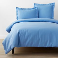 a bed with blue sheets and pillows on top of wooden floor next to white wall