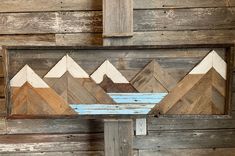 a wooden sign with mountains painted on it's side in front of a wood wall