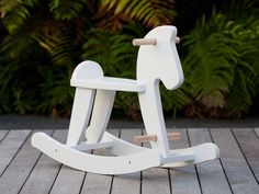 a white rocking horse toy sitting on top of a wooden floor next to green plants