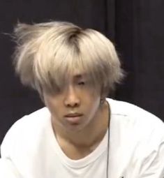 a young man with blonde hair sitting in front of a black background wearing a white t - shirt