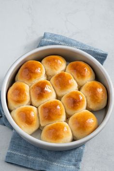 a white bowl filled with bread rolls on top of a blue cloth next to a napkin