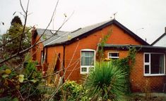 a red brick house sitting next to a lush green yard with trees and bushes in front of it