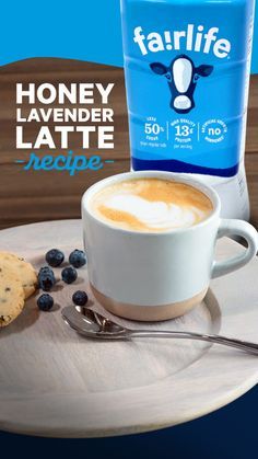 a cup of latte next to a bottle of milk and some blueberries on a plate