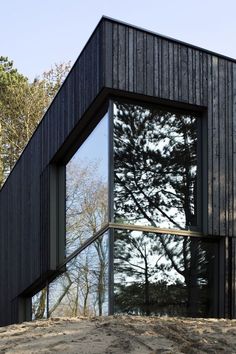 the side of a black building with trees in the back ground and sky reflected in the windows