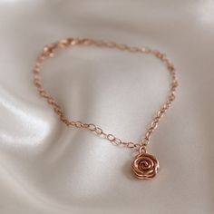 a gold bracelet with a rose on it sitting on a white fabric background, close up