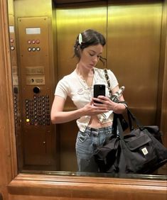 a woman standing in an elevator looking at her cell phone and holding a black bag