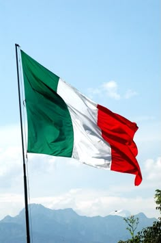 the italian flag is flying high in the blue sky with mountains in the back ground