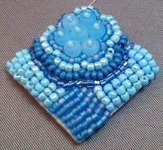 a blue beaded brooch sitting on top of a piece of cloth covered in beads