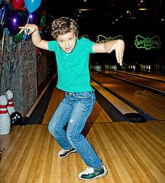 a young boy is bowling in a bowling alley with balloons and streamers all around him