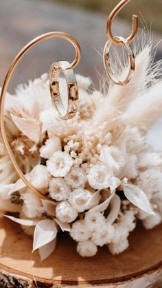 the wedding rings are sitting on top of some white flowers and feathers in front of a wooden stand