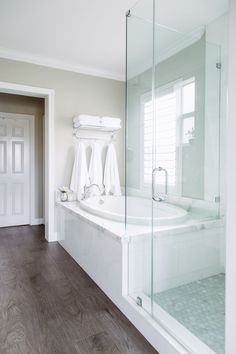 an empty bathroom with wood flooring and white fixtures on the shower door, tub, and toilet