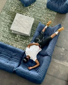 a man laying on top of a blue couch next to a green rug and pillows