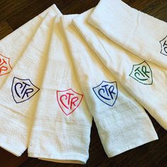 five white towels with different colored monogrammed initials on them sitting on a wooden floor