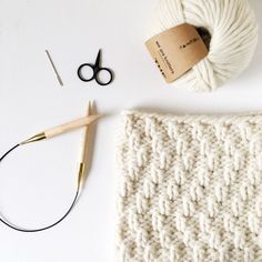 yarn, scissors and knitting needles on a white surface