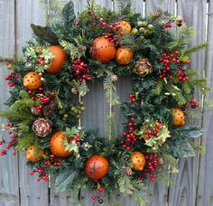 a christmas wreath with oranges and berries hanging from it's side on a wooden fence