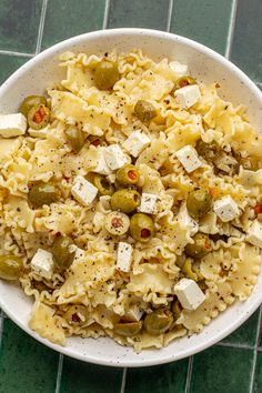 a white bowl filled with pasta and olives on top of a green tile floor