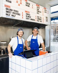 two men in blue aprons standing behind a counter