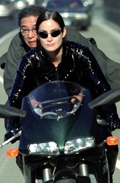 a man and woman riding on the back of a motorcycle