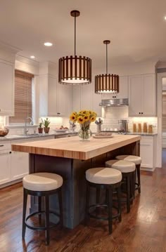 a kitchen island with four stools in front of it and sunflowers on the counter