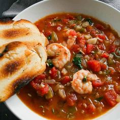 a white bowl filled with shrimp and vegetable soup next to a piece of toasted bread