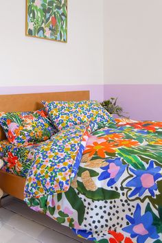 a bed with colorful bedspread and pillows in front of a painting on the wall