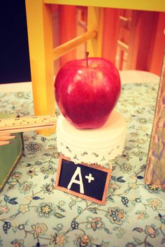 an apple sitting on top of a wooden block next to a ruler and pencils