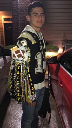 a man standing next to a red car holding a football fan's jersey and trophy