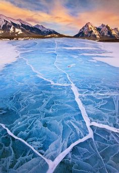 an ice covered lake with mountains in the background and water flowing down it's sides