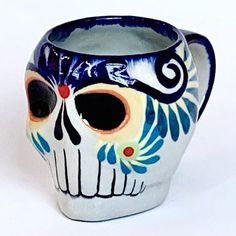 a white and blue skull mug with eyes painted on it's side, sitting in front of a white background